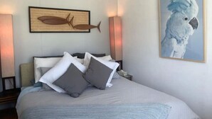 A neatly made bed with pillows, a framed fish artwork, and a parrot painting on the wall. - Cosy retro styled bungalow (Mollymook Beach)