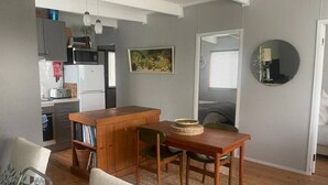 A compact living space with a kitchenette, a dining area with a wooden table and chairs, and a small seating area with a chair and a sofa. - Cosy retro styled bungalow (Mollymook Beach)