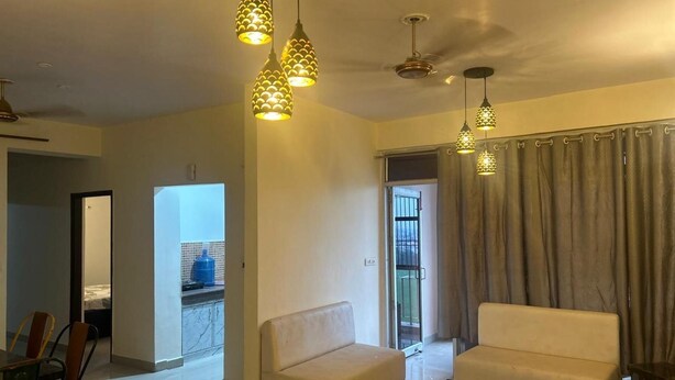 A spacious living room with a sofa, a coffee table, and pendant lights. There is a sliding door leading to a balcony. - Highriseviews/familyfriendly/neartajmahal (Agra)