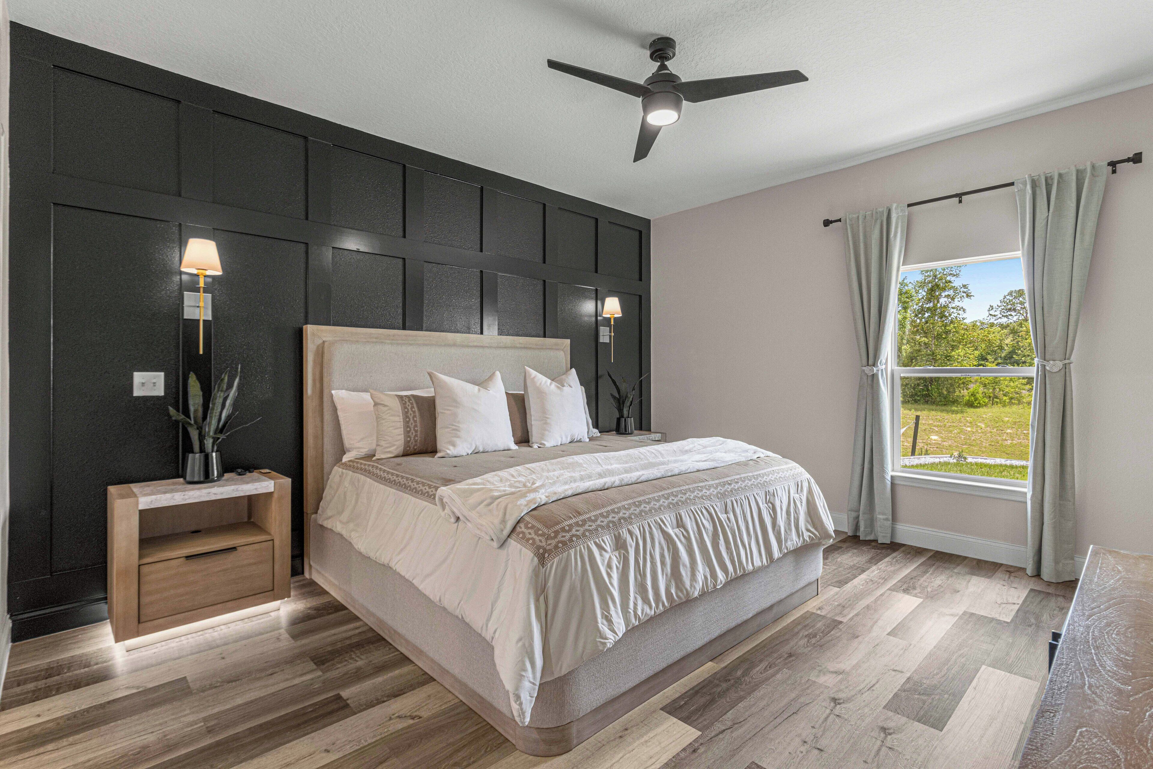 Quarto com cama grande, luminárias de cabeceira, ventilador de teto e vista para o verde pela janela.