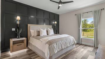Quarto com cama grande, luminárias de cabeceira, ventilador de teto e vista para o verde pela janela.