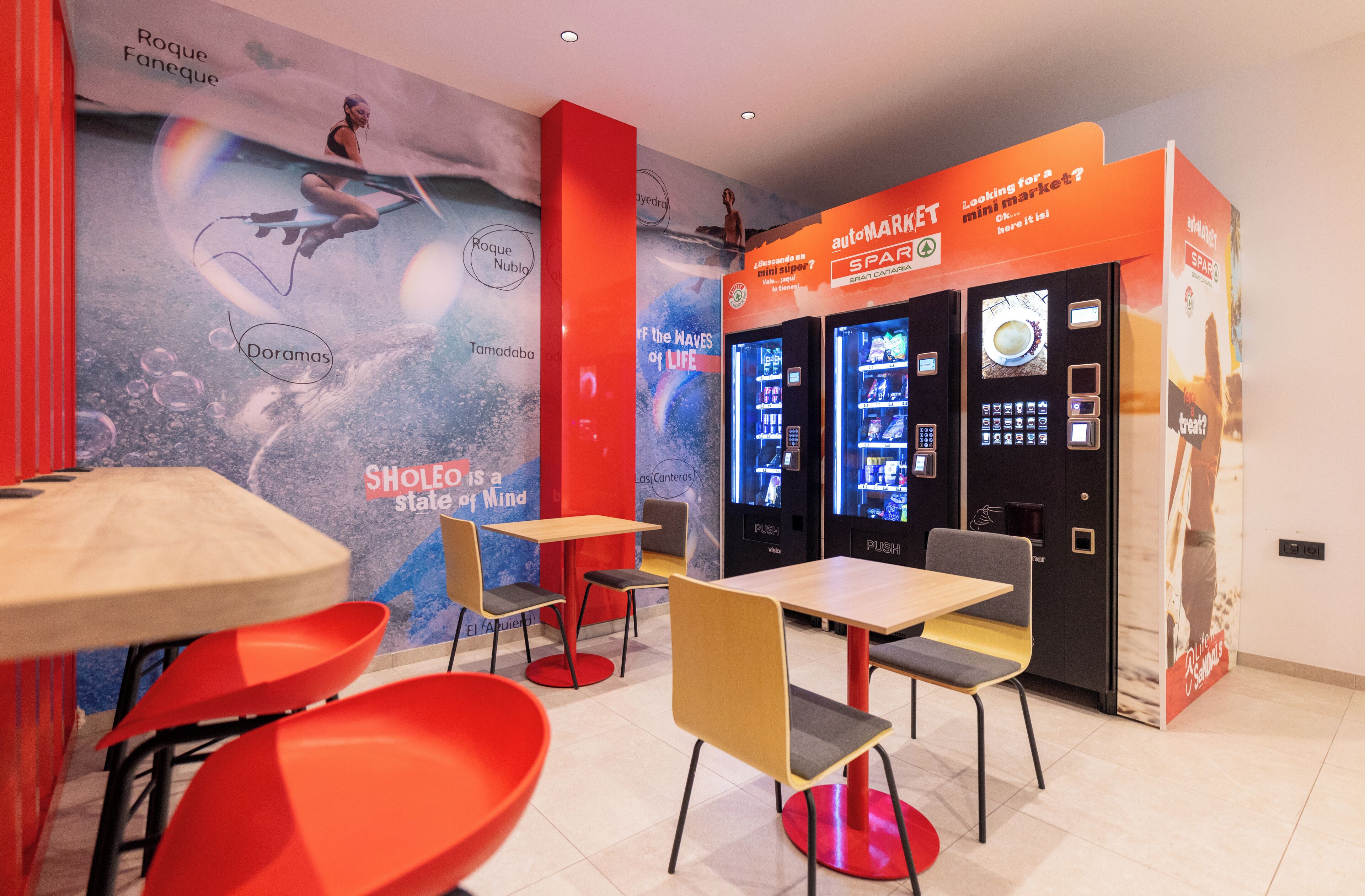 A modern cafe interior with seating, vending machines, and a mural.