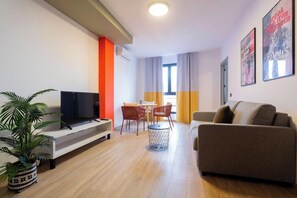 Una sala de estar moderna con un televisor de pantalla plana, un sofá, una mesa de comedor con sillas y una planta en maceta.