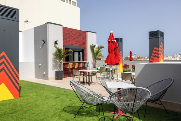 An outdoor patio with tables and chairs, a red umbrella, and a view of the city. - Sholeo Lodges Las Palmas Flats (Las Palmas de Gran Canaria)