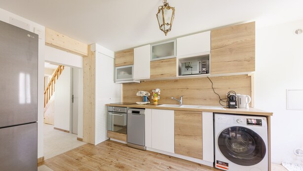 A modern kitchen with a stainless steel refrigerator, dishwasher, and washing machine, wooden cabinets, and a wooden floor. - L'Arverne du Rocher - Maison vue montagne (La Bourboule)