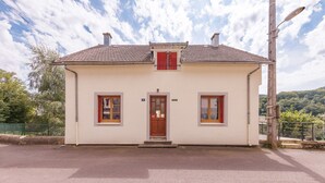 A single-story building with a tiled roof, a central entrance, and two windows with shutters. - L'Arverne du Rocher - Maison vue montagne (La Bourboule)