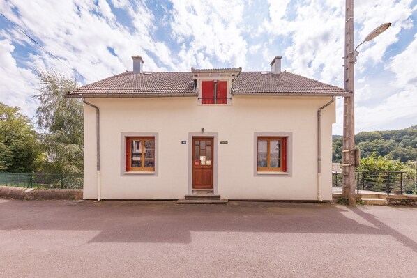 A single-story building with a tiled roof, a central entrance, and two windows with shutters. - L'Arverne du Rocher - Maison vue montagne (La Bourboule)