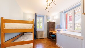 A room with bunk beds, a radiator, a wooden cabinet, a table, and a window with curtains. - L'Arverne du Rocher - Maison vue montagne (La Bourboule)