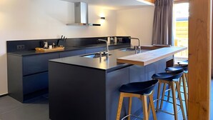 A modern kitchen with a central island, bar stools, and a view of the outdoors.