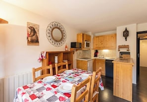 A compact kitchen with wooden cabinets, a microwave, a dishwasher, and a dining area with a table set for two.