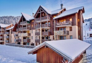 Un chalet en bois à plusieurs étages, doté de balcons, qui se dresse sur fond de montagnes enneigées.