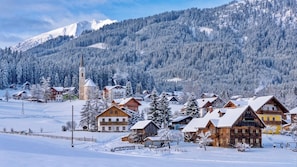 A snow-covered village with wooden houses, a church, and mountains in the background.