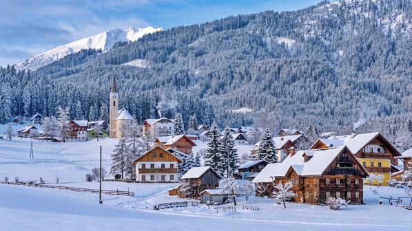 A snow-covered village with wooden houses, a church, and mountains in the background.