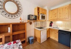 A compact kitchen with wooden cabinets, a microwave, a coffee maker, and a dishwasher.