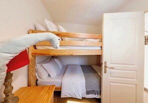 A bunk bed with white bedding, a wooden headboard, and a small bedside table with a lamp.