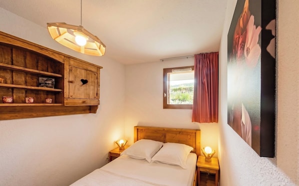 Un dormitorio con cabecera de madera, una mesita de noche con lámpara, una ventana con vistas y un mueble de pared con adornos.