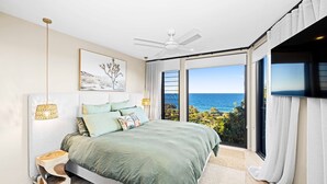 Ein Schlafzimmer mit einem Bett, einem Deckenventilator, einem großen Fenster mit Meerblick und einem flachbildfernseher an der Wand.