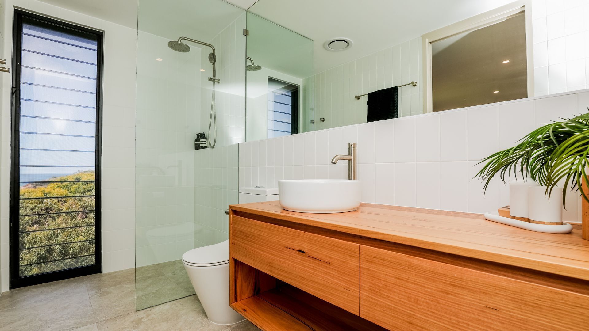 A modern bathroom with a glass shower enclosure, a white sink, and a wooden vanity.