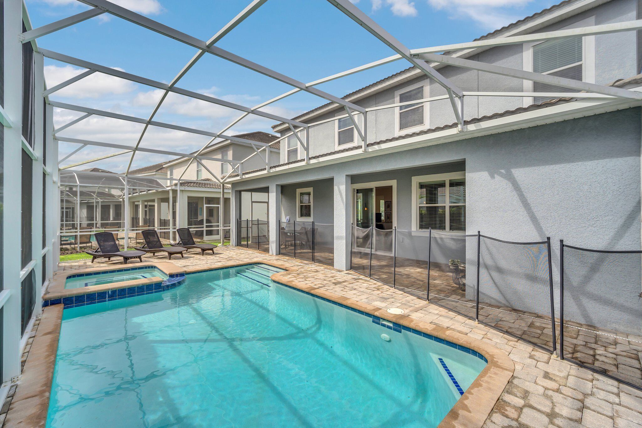 A covered swimming pool with lounge chairs and a fenced area.
