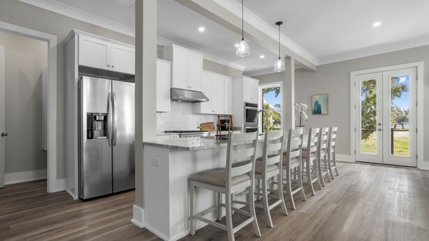 A modern kitchen with white cabinetry, stainless steel appliances, and a bar area with chairs.