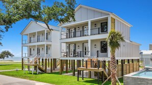 A two-story waterfront house with a balcony, a pool, and a view of the ocean.