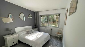 A bedroom with a bed, bedside tables, a chair, a window with a view of greenery, and a radiator. - Cosy apartment, 5 minutes from La Baule beach (La Baule-Escoublac)