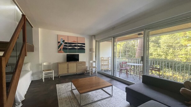 A modern living room with a sofa, a coffee table, a TV on a wooden cabinet, and a balcony with a view of trees. - Cosy apartment, 5 minutes from La Baule beach (La Baule-Escoublac)