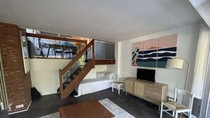 A modern living room with a staircase, a white sofa, a coffee table, a TV, and a painting on the wall. - Cosy apartment, 5 minutes from La Baule beach (La Baule-Escoublac)