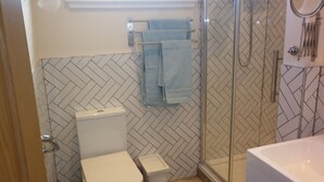 Et badeværelse med toilet, bruseniche med glasdør og badekar.
