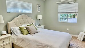 Une chambre à coucher avec un grand lit, deux tables de chevet, un climatiseur fixé au mur et une fenêtre avec des stores.