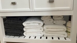 Un meuble blanc avec deux tiroirs et une étagère. L’étagère contient des serviettes blanches et grises, soigneusement pliées.