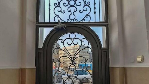 Une porte en métal noir ornée de motifs complexes, qui mène à l’entrée d’un bâtiment.