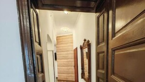 Un couloir doté d’un plancher et de portes en bois, qui mène à une pièce avec un mur lambrissé et un luminaire au plafond.