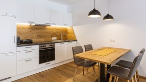 A modern kitchen with white cabinets, a wooden countertop, a built-in oven, and a dining table with chairs. - Apartment for up to 2 Adults and 2 Children (Turrach)