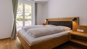 A bedroom with a wooden bed, a headboard with a light fixture, a bedside table, and a window with curtains. - Apartment for up to 2 Adults and 2 Children (Turrach)