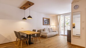 A modern living room with a wooden dining table, grey chairs, a beige sofa, and a large window with curtains. - Apartment for up to 2 Adults and 2 Children (Turrach)