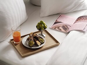 A tray with a glass of orange juice, a plate of pastries, and a bowl of green fruits on a bed with pillows and an open magazine. - Mekano Apartment Hotel (Copenhagen)