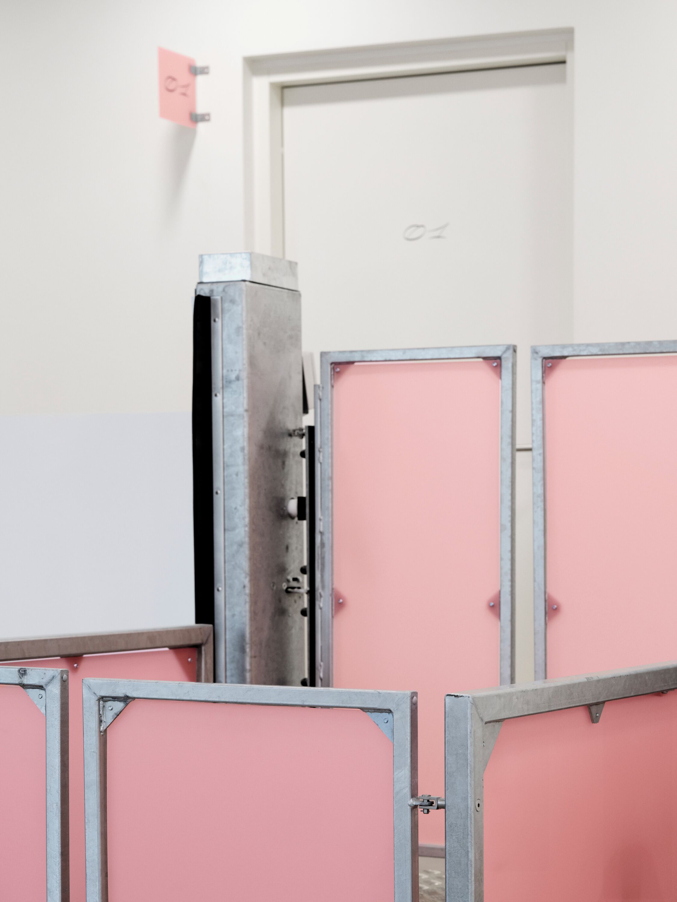 Un conjunto de taquillas metálicas con puertas rosas, una pared blanca y una puerta con un número.