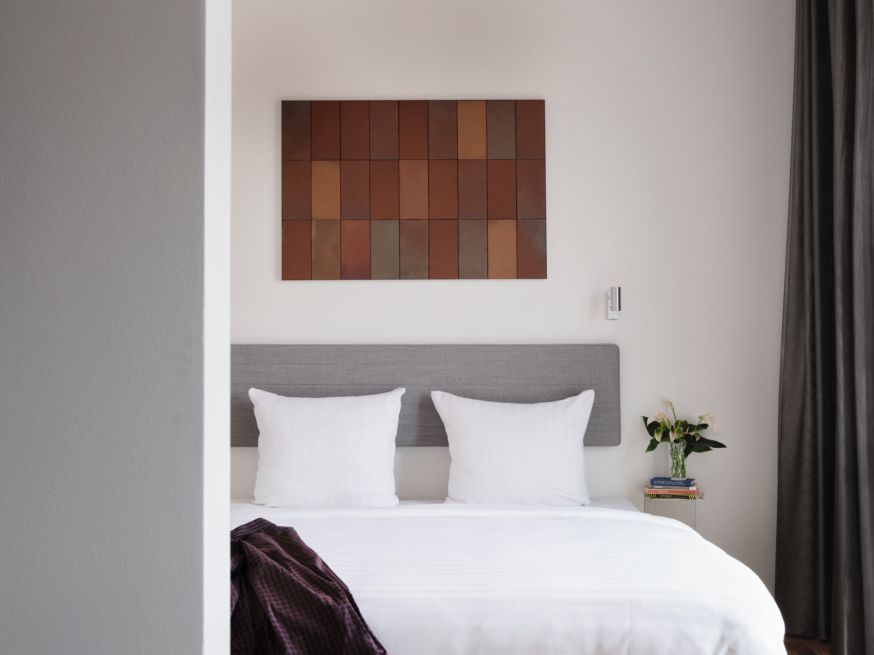 A neatly made bed with white linens and two pillows, a grey headboard, and a wall-mounted artwork above it.