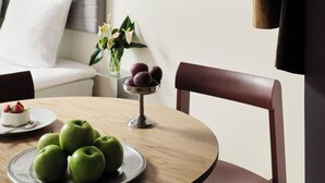 Ein modernes Wohnzimmer mit einem runden Holztisch, einem grauen Sofa, einem großen Spiegel und einer Pendelleuchte.