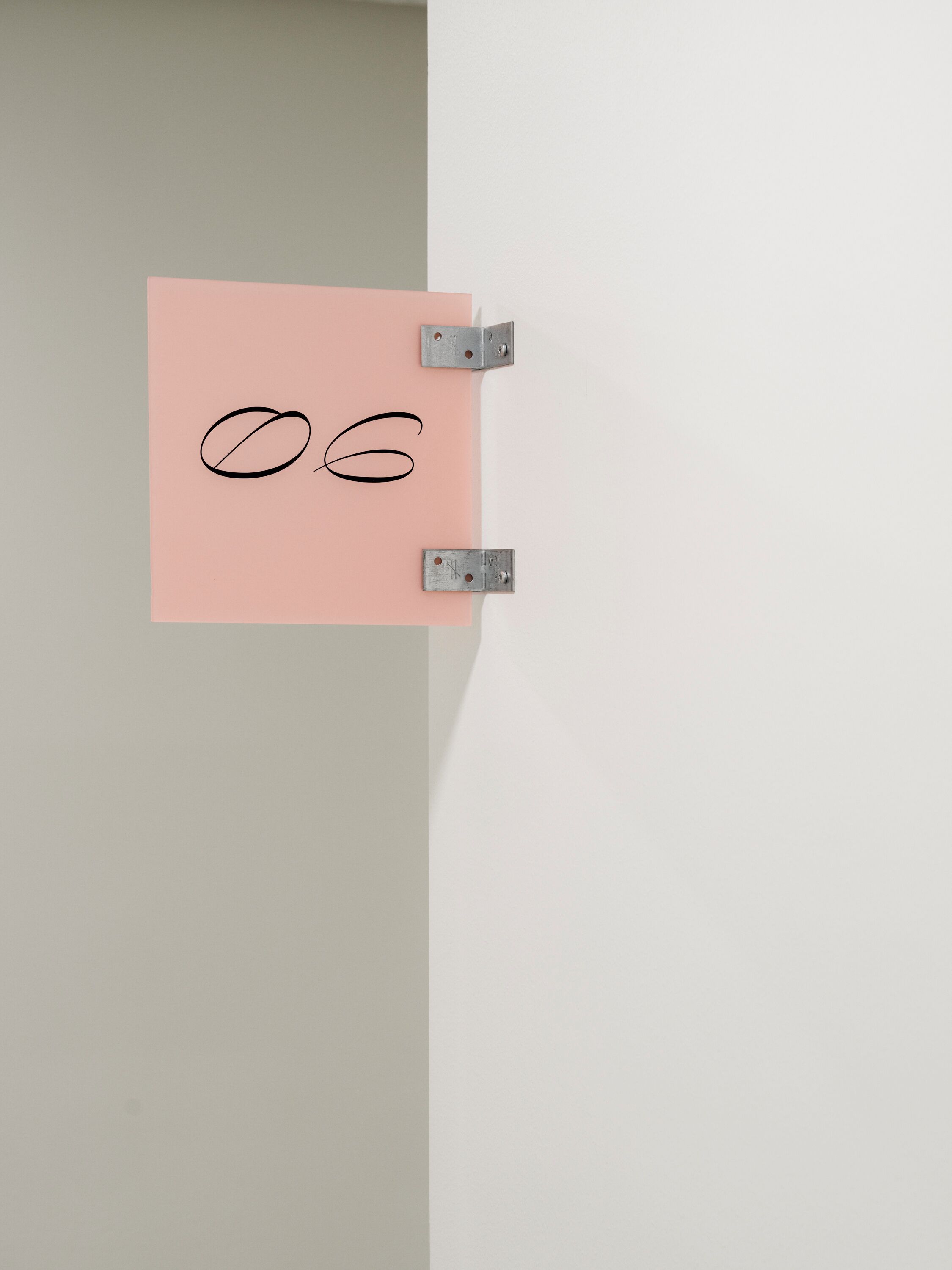 Um post-it rosa com o número 06 escrito, preso a uma parede por suportes metálicos.