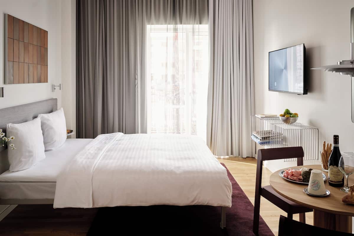 Une chambre d’hôtel avec un lit, une table à manger avec une bouteille de vin et un téléviseur fixé au mur.