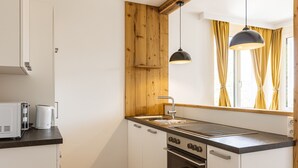Cozinha compacta com parede de destaque em madeira, forno embutido e luminária pendente preta.