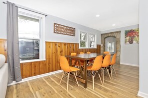 A dining area with a wooden table and orange chairs, a 'welcome' sign, and a stone archway.