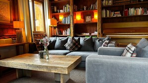 A cozy living room with a wooden coffee table, a sofa, and a bookshelf filled with books and decorative items. - Sycamore Alpine Retreat - 5 mins from the slopes (Les Belleville)