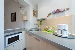 Compact kitchen with oven, sink, and coffee maker, featuring light-colored cabinetry and decorative accents.