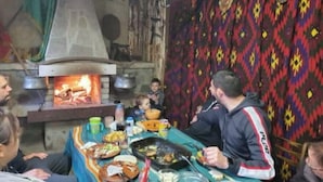 Un coin repas rustique avec un poêle à bois, une table dressée avec différents plats et un rideau à motifs en arrière-plan.