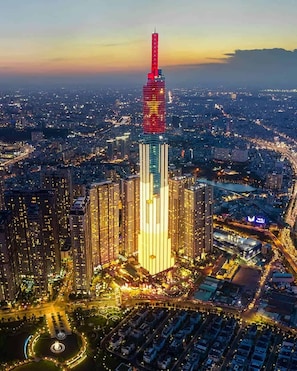 A high-rise building with a distinctive red and blue top, surrounded by a cityscape at dusk. - Vinhomes Central Park Premier Apartment (Ho Chi Minh City)