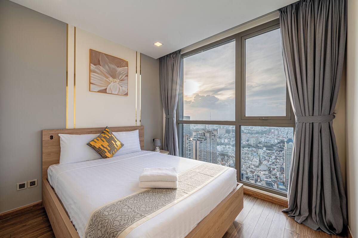 A modern hotel room with a large bed, a city view, and a large window with curtains.