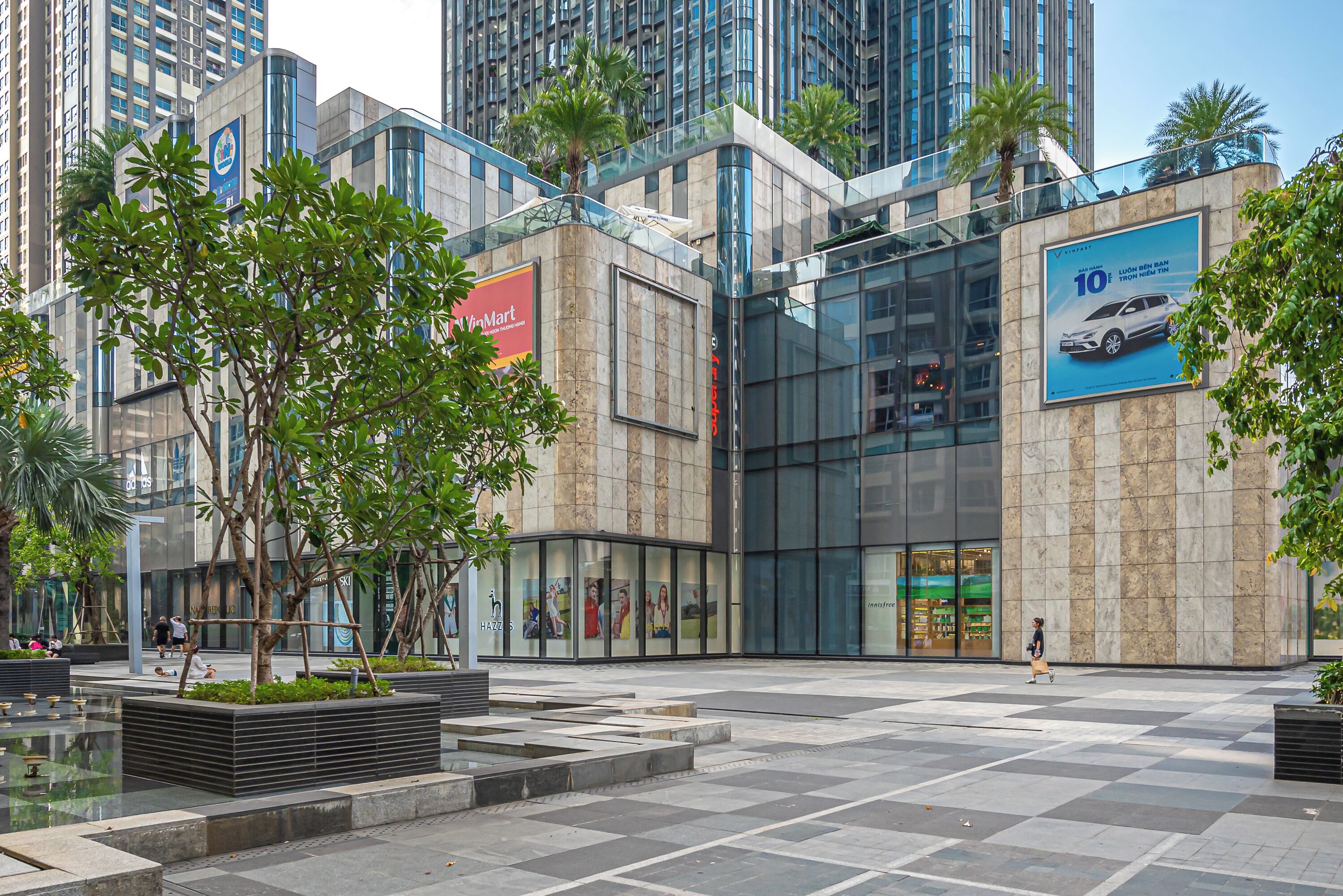 A modern urban plaza with a large glass building, a McDonald's sign, and a car advertisement.